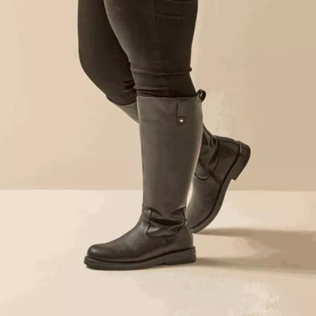 Modèle portant des Bottes cavalières mollets larges 3XL Lise - Gabylou en noir, jumelées à un legging noir, debout, un pied croisé devant l'autre. Mode Grande taille