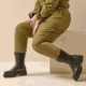 Personne en combinaison olive assise, présentant les Bottines à clous pour pieds larges 2XL Jade by Gabylou - bottes noires cloutées à semelles épaisses - sur un fond beige. Mode Grande taille