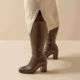Une personne portant les Bottes à talon mollets larges 4/5XL Gladys - Gabylou, des bottes brunes à talon au niveau du genou, associées à une jupe beige avec une fente sur le devant. Mode Grande taille
