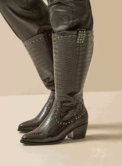 Bottes santiag mollets larges 3XL Thelma - Gabylou, en simili cuir noir à imprimé crocodile, talons blocs et détails cloutés, portées sur un pantalon noir. Mode Grande taille