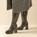 Les Bottes à talons mollets larges 3/4XL Manon-Gabylou, avec une texture et des talons en crocodile noir, se portent sous un manteau gris, à partir des genoux. Mode Grande taille