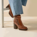 Une personne portant des Bottines à talons 2XL Kim - Gabylou et un jean bleu est assise sur une chaise en bois blanc. Mode Grande taille
