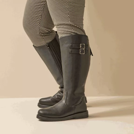 Personne portant un pantalon à motifs et Laure - Gabylou Bottes cavalières mollets larges 5/6XL, des bottes noires au genou avec des boucles latérales, debout sur un sol de couleur claire. Mode Grande taille