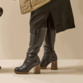 Femme portant des Bottes mollets larges 2XL Mélissa - Gabylou, des bottes en cuir noir à talons hauts et une jupe noire ; patte de chien visible à gauche. Mode Grande taille