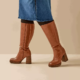 Modèle portant des Bottes mollets larges 2XL Mélissa - Gabylou en marron avec une jupe en denim bleu, sur fond beige. Mode Grande taille