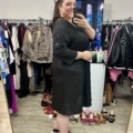 Une femme sourit dans un selfie au miroir, portant l'anneau décolleté de la Robe noire, entourée d'étagères et de chaussures dans un magasin de vêtements. Mode Grande taille