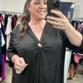 Une femme sourit et prend un selfie dans un magasin de vêtements en portant l'anneau Robe noire décolleté. Mode Grande taille