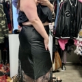 Une femme sourit en prenant un selfie dans un magasin de vêtements en portant le Jupe satin dentelle noire. Mode Grande taille