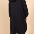 Une personne portant la Robe col chemise fendue sur les côtés et des bottes noires, vue de dos sur fond beige. Mode Grande taille