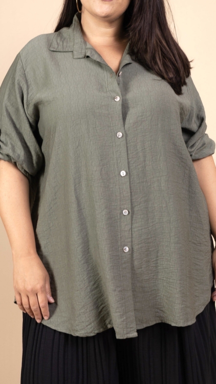 Une personne portant la Chemise en viscose, une chemise à boutons vert olive avec des manches roulées, associée à un pantalon noir. Mode Grande taille