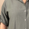 Gros plan d'une personne portant la Chemise en viscose, une chemise verte boutonnée aux manches retroussées, sur un fond beige. Mode Grande taille