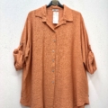 Chemise ample en viscose de couleur orange avec manches à revers, boutonnée sur le devant, exposée sur un cintre contre un mur blanc. Mode Grande taille