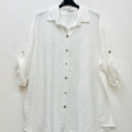 Chemise en viscose blanche à manches longues, boutonnée, avec col, suspendue sur un cintre noir devant un mur blanc. Mode Grande taille