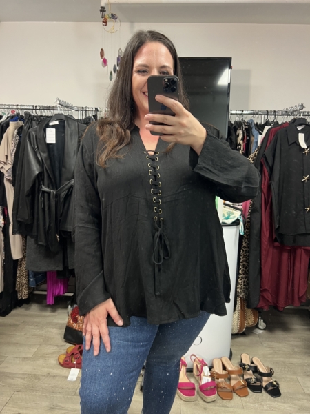 Femme prenant un selfie dans un magasin de vêtements, portant la Blouse à laçage noire et un jean bleu. Mode Grande taille
