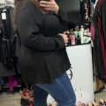 Une femme sourit et prend un selfie dans un magasin de vêtements, portant la Blouse à laçage noire, entourée de chaussures et de vêtements. Mode Grande taille