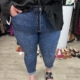 Une personne porte la Jean à strass, associée à un haut noir et à des sandales, debout dans un magasin de vêtements avec des chaussures exposées en arrière-plan. Mode Grande taille