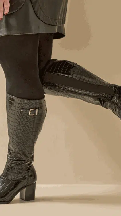 Personne portant Bottes à talons pour mollets larges 3XL Romy croco noir - Gabylou et des collants noirs, debout, une jambe pliée au niveau du genou. Mode Grande taille