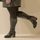Personne portant Bottes à talons pour mollets larges 3XL Romy croco noir - Gabylou et des collants noirs, debout, une jambe pliée au niveau du genou. Mode Grande taille