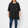 Blouse grande taille noire col rond avec boucle dorée, portée par une femme ronde